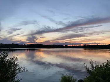 a body of water with trees and a sunset in the background