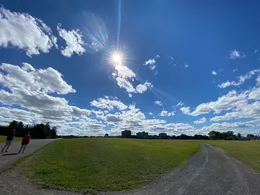 a road with grass and people on it and a blue sky with clouds