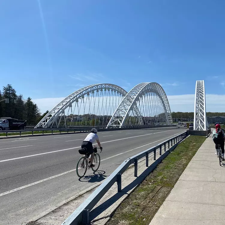 a group of people riding bikes on a road with a bridge in the background